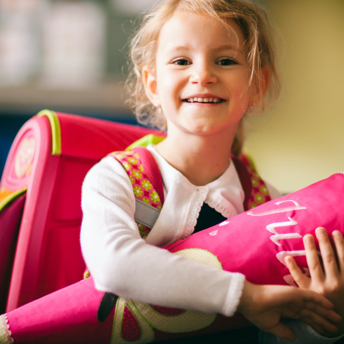 Ein glücklich lächelndes Mädchen mit einer Pinken Schultüte im Arm und passender Schultasche auf dem Rücken