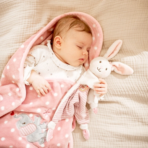 friedlich schlafendes Baby auf einer rosa Plüschdecke mit einem Kuschelhäschen im Arm.