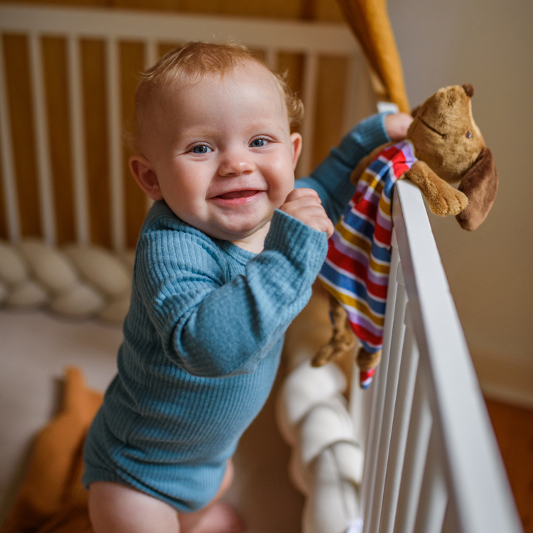 Lachendes Baby im Laufstall mit Dackel-Schnuffeltuch.