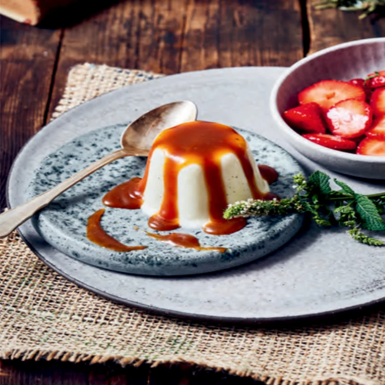 Gestürzter Pudding mit hellbrauner Soße angerichtet auf rustikalen Keramiktellern und einem Leinendecken auf einem alten Tisch.